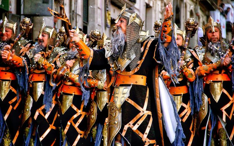 Deelnemers in kleurrijke kostuums tijdens een optocht van Moros y Cristianos