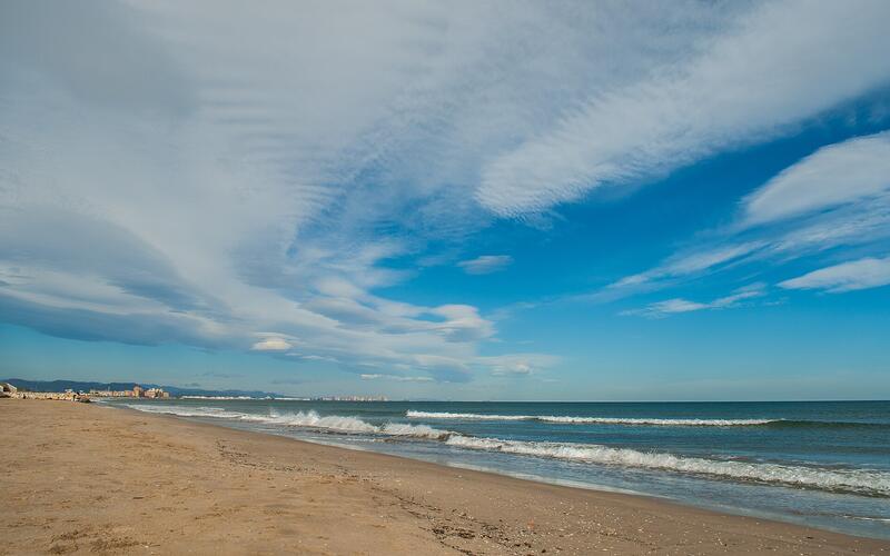 Breed zandstrand aan de Middellandse Zee bij Valencia onder een blauwe lucht met wolken